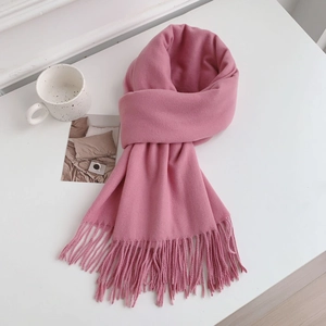 Detail of soft pink cashmere-style scarf with tassel fringe on a cozy white desk setup