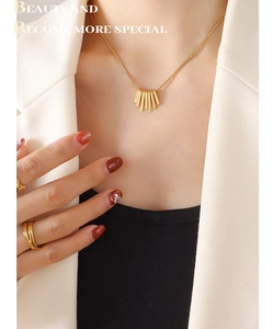 Detail of gold fringe square pendant necklace and layered rings on female model