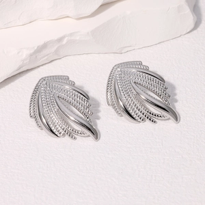 Minimalist silver wing earrings with textured feathers on white stone surface