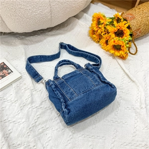 Detail of blue denim crossbody bag with adjustable strap on white textured background