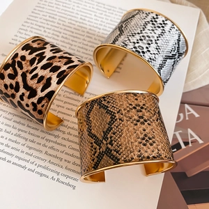 Detail of three wide open cuffs with leopard and snake skin patterns in gold finish