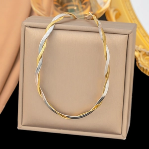 Elegant gold and silver braided chain necklace set on a beige leather jewelry box surface