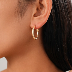 Close-up of a minimalist golden hoop earring worn on model's ear with polished finish