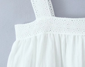 Dettaglio in primo piano di tessuto in cotone bianco con ricamo sangallo e spalline sottili