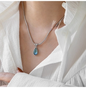 Detail of silver teardrop necklace with deep blue gemstone on a white shirt