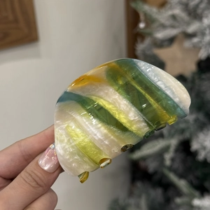 Detail of candy-colored acetate hair claw clip with striped texture in a hand-held shot
