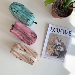 Three-piece corduroy pouches in pink, green, and beige with smiley faces on a flat surface