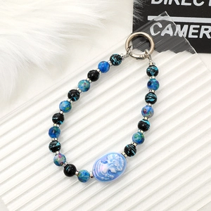 Macro detail of a blue cameo beaded charm strap with silver hardware on white textured fur