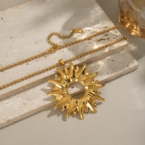Elegant gold stainless steel necklace with sunburst pendant on a textured stone base