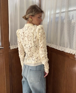 Detalle de la blusa de encaje blanco crema con motivos florales y corte entallado
