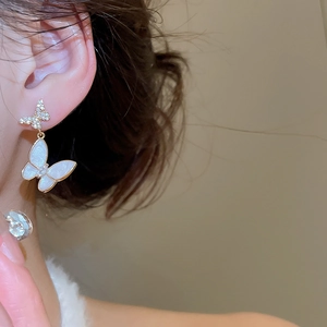 Close-up of model wearing gold-tone butterfly drop earrings with white shell and zircon