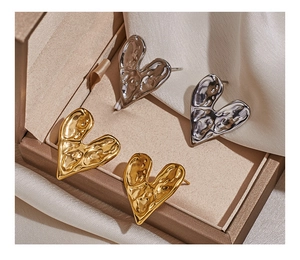 Close-up of gold and silver heart studs with lava texture on beige silk background
