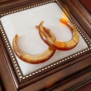 Close-up of amber resin C-shaped earrings with marble texture on fabric background