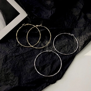 Close-up of gold and silver large hoop earrings with textured finish on black backdrop