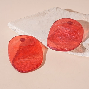 Macro detail of red resin irregular circle earrings on a grey stone texture base