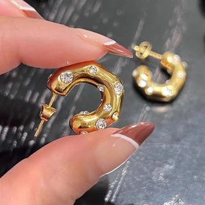 Close-up of chunky gold-plated C-hoop earrings with round zircon stones held by a hand