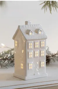 Warm glowing light through windows of white ceramic house decor on Christmas pine needles