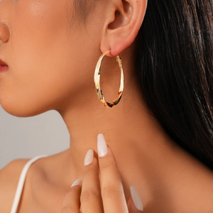 Close-up of model wearing twisted gold hoop earrings with a minimalist metallic finish