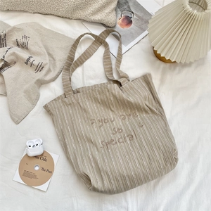 Detail view of striped canvas tote bag with embroidered slogan and natural cotton texture