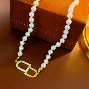 Détail macro du collier ras du cou en perles avec pendentif CD doré serti de zircons
