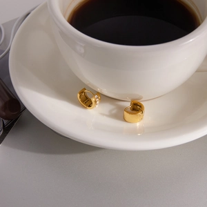 Close-up of gold-plated hoop earrings with micro-paved zircons on a white ceramic plate