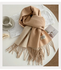 Close-up of dual-tone beige scarf with tassel details and minimalist brand label