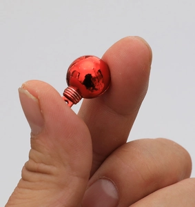 Dettaglio di una mini pallina di Natale rossa lucida da 1,5 cm tenuta tra due dita