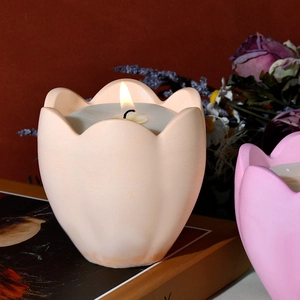 Vista detallada de vela aromática de 6 pétalos encendida en recipiente de yeso mate tipo tulipán