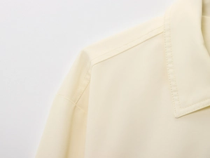 Detailed close-up showing the fine stitching and texture of the cream bomber jacket fabric