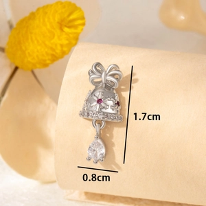 Silver bell earring with bow design, red gem, and drop crystal on textured surface