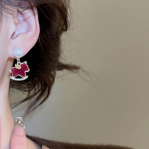 Close-up of red rocking horse earring with pearl accent and sparkling crystals on model