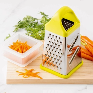 4-sided stainless steel box grater with yellow handle on a wooden board with carrots
