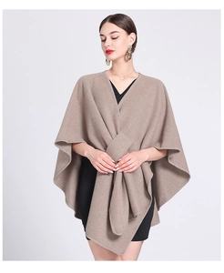 Detail of a beige knit poncho wrap styled over a black dress for women's winter fashion