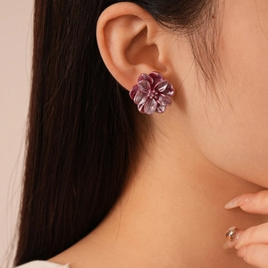 Gros plan de boucles d'oreilles fleurs en résine bordeaux portées par un modèle