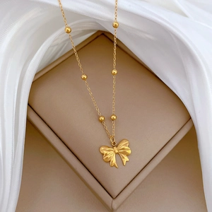 Detailed close-up of a gold bow pendant necklace with beads on a jewelry gift box