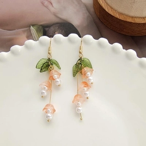 Detail of pink lily of the valley earrings with green leaves and pearls on white plate