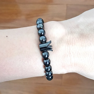 Detailed close-up of a men's black beaded crown bracelet worn on a wrist over wood