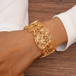 Macro shot of wide matte gold hollowed floral cuff bracelet on wrist over wood