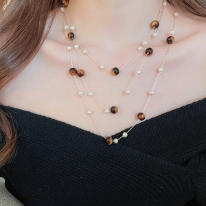 Détail d'un collier doré multicouche avec pierres œil de tigre vintage et perles blanches