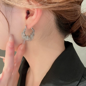 Detailed close-up of a silver radiating spike hoop earring worn on a female model