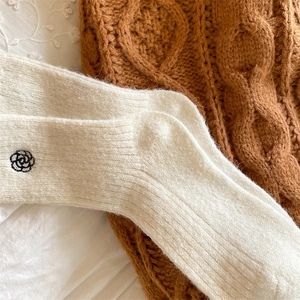 Close-up of cream winter wool socks with delicate black flower embroidery detail