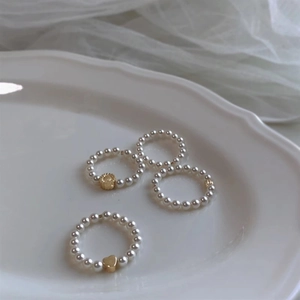 Detail shot of four pearl rings with gold beads and heart accents on a white plate