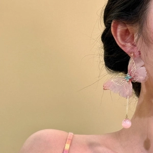 Close-up detail of oversized pink mesh butterfly tassel earrings on model