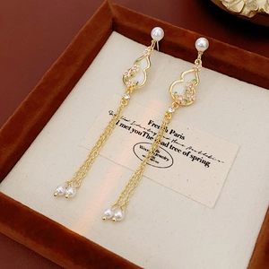 Detailed macro view of gold gourd earrings with pearl tassels and enamel flowers