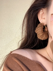 Detail of a brown knitted wool hoop earring worn by a model in a warm retro style
