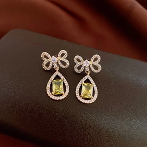 Close-up of golden bow earrings with yellow rectangle stone and teardrop frame detailing
