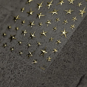 Macro shot of gold star-shaped embossed nail art stickers on a textured gray background