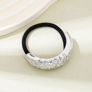 Detail view of a silver textured metal cuff hair tie on a minimalist beige background