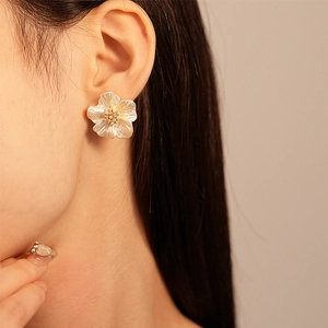 Close-up of model wearing white acrylic flower earrings with pearl and gold zircon details