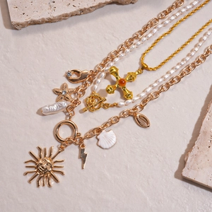 Detail of layered gold chains with pearl strand, sun face and vintage cross charms